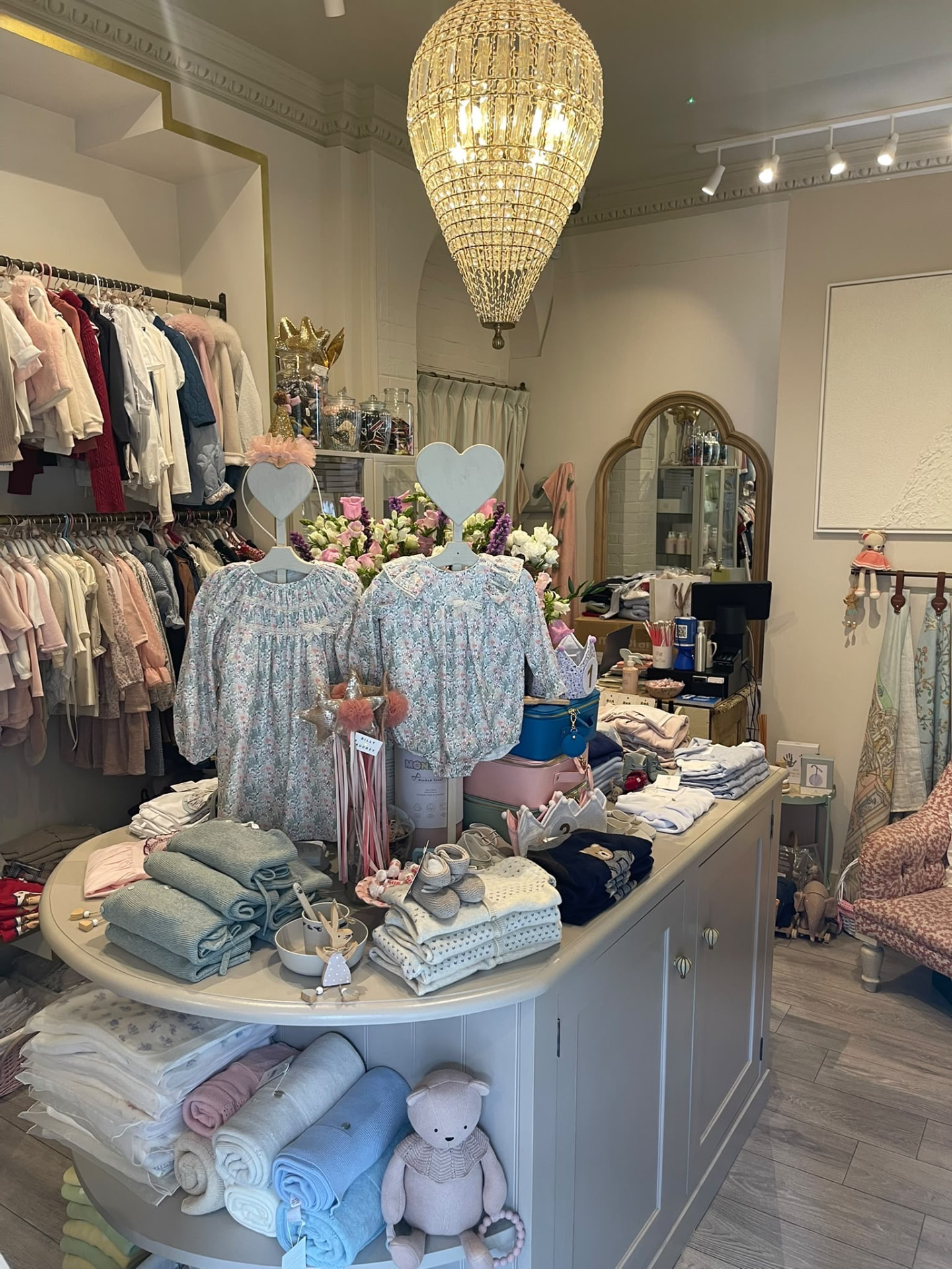 Inside the Petit BonBon boutique with a chandelier, floral dresses on heart hangers and soft knits folded on the round table